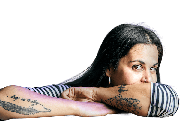 Una persona con cabello largo y aros apoya sus brazos sobre una superficie, mostrando tatuajes en ambos antebrazos.