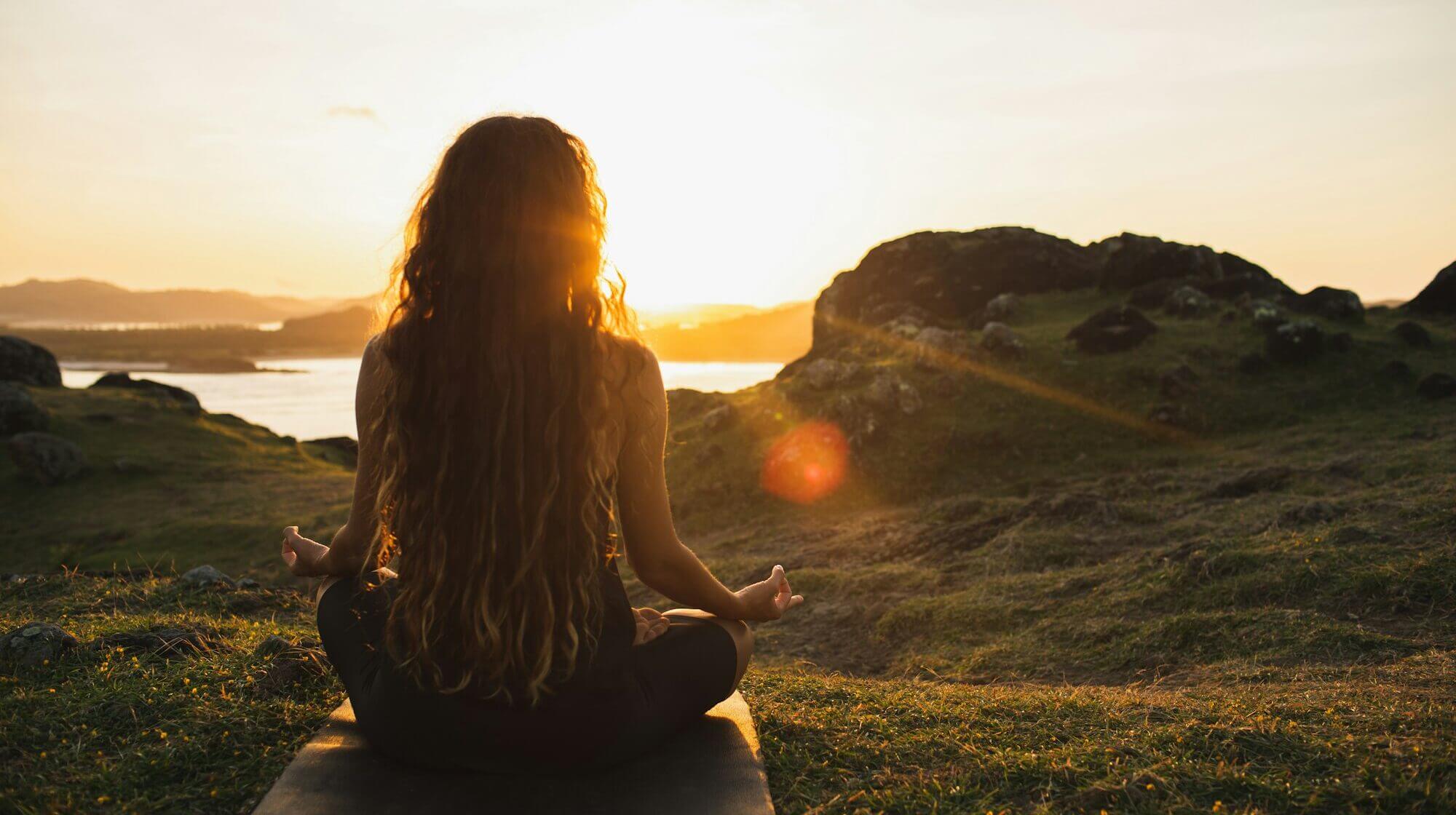 Woman meditating yoga alone at sunrise mountains. View from behind. Travel Lifestyle